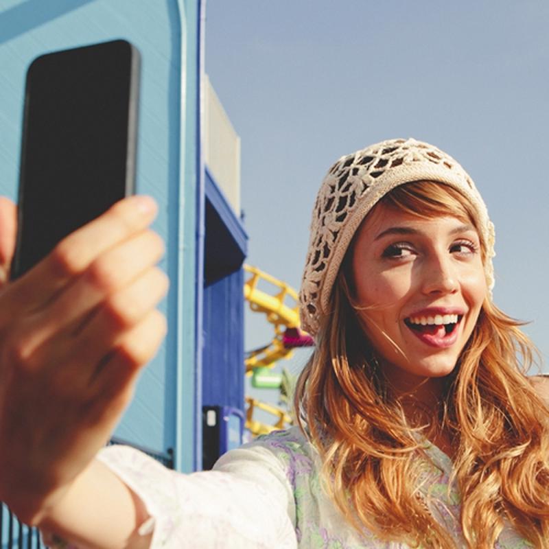 A young woman is pictured taking a photo of herself; a selfie. 