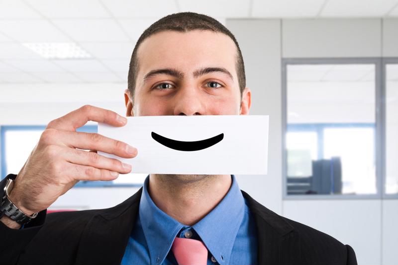 A businessman holds a smiley face card in front of his mouth