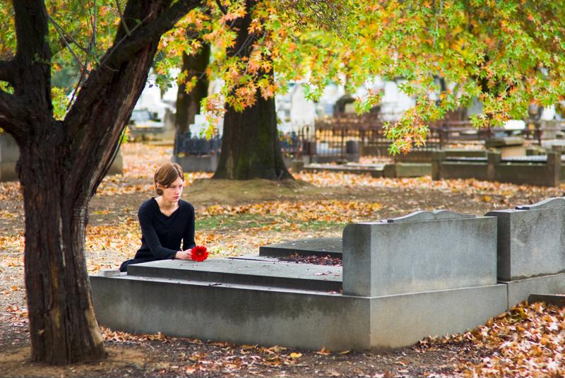 Mourning woman with flower at gravesite. 