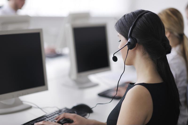 Woman in black sleeveless top working in call center, wearing telecom headset and typing on keyboard