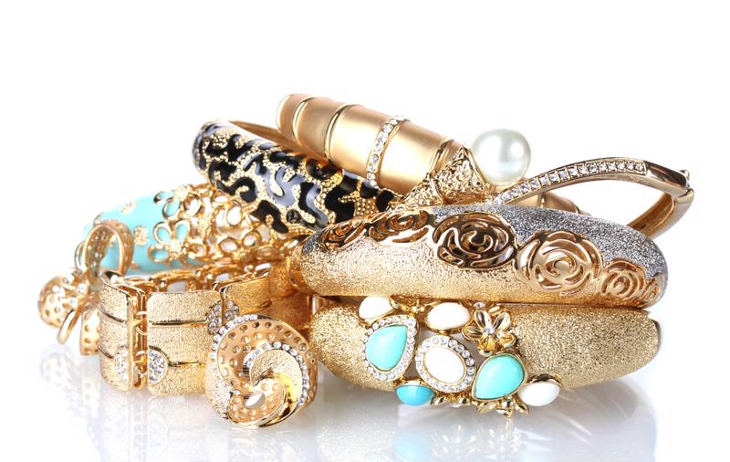 Gold jewelry with diamonds and gems lie in a pile on a table.