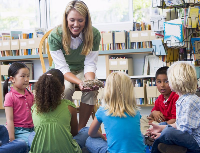 A teacher in the library shows something to a circle of young students