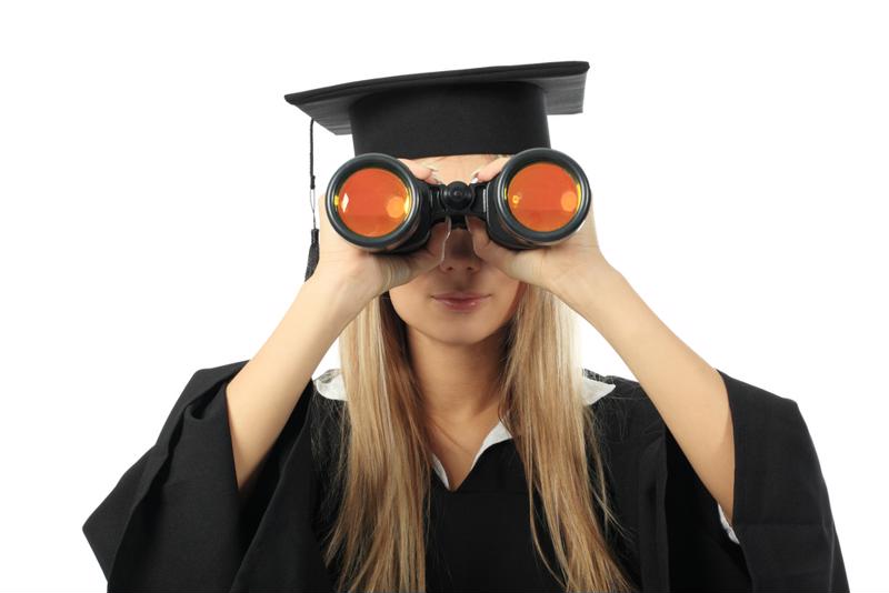 Female in graduation gown and gap looking through binoculars.