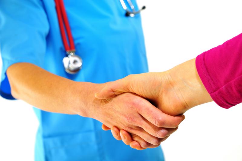 Person in scrubs and a stethoscope shaking hands with another person. 