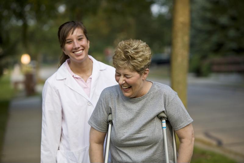 Occupational therapist helping older adult walk on crutches.