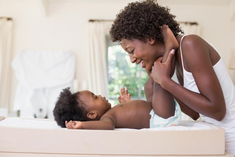 African American mom with baby on changing table, baby wearing a diaper. 