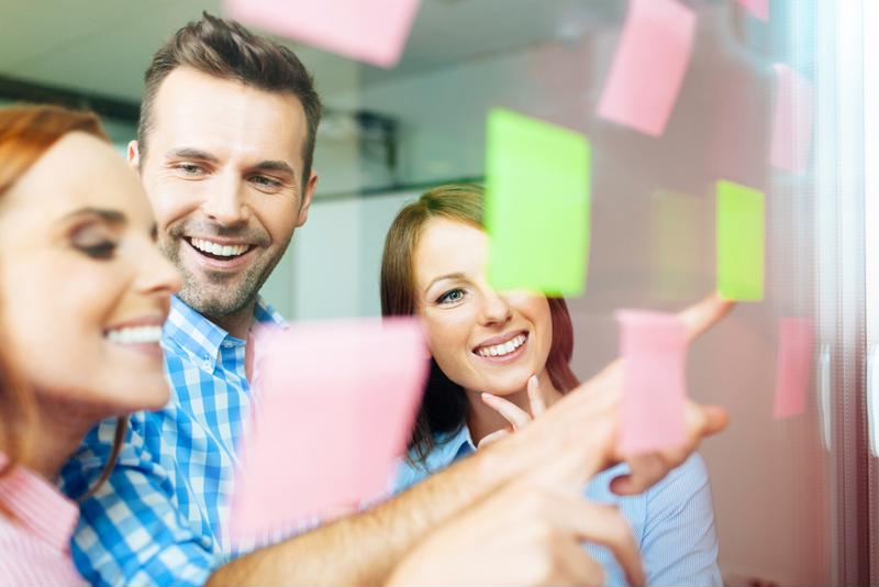 Three employees look happily at sticky notes on the wall