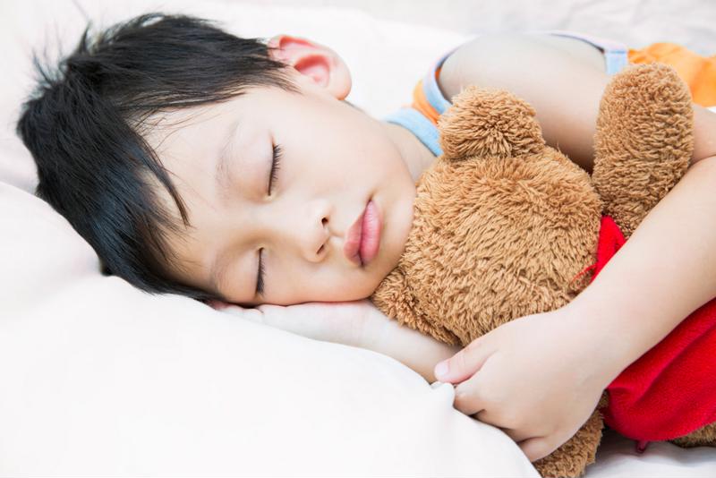 A little boy sleeping and holding a teddy bear.