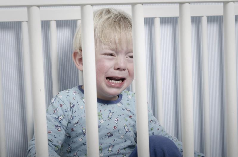 A baby boy crying in a crib.