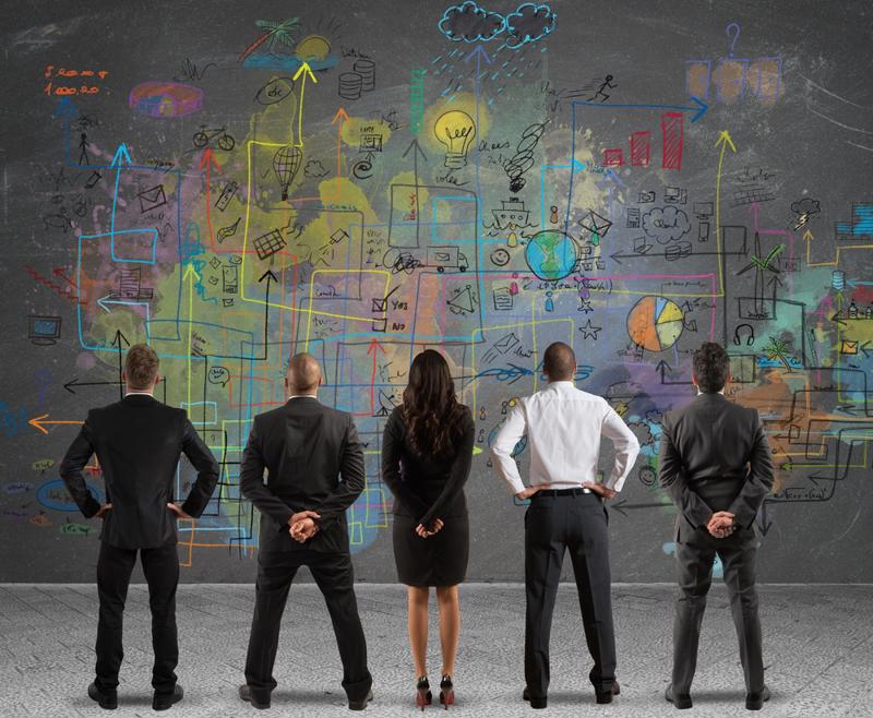 Team members view a wall of diagrams.