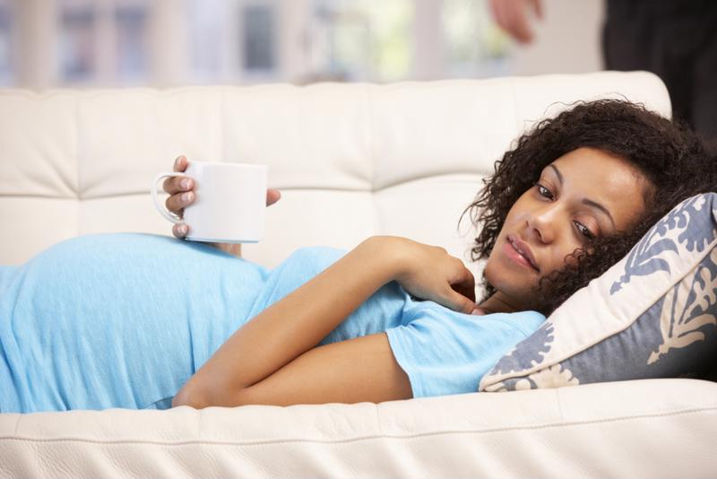 Pregnant woman laying on a sofa holding a mug.
