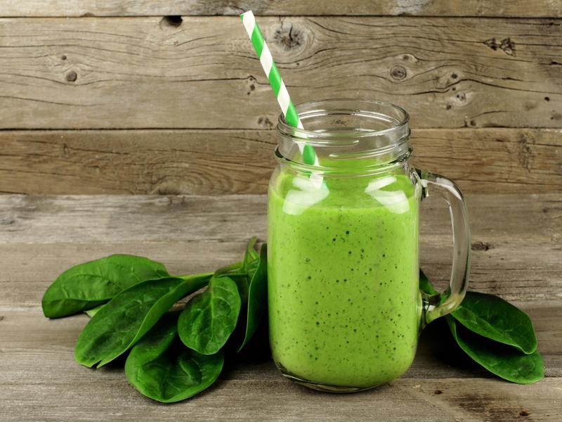 A green smoothie in a mason jar next to a bundle of spinach.