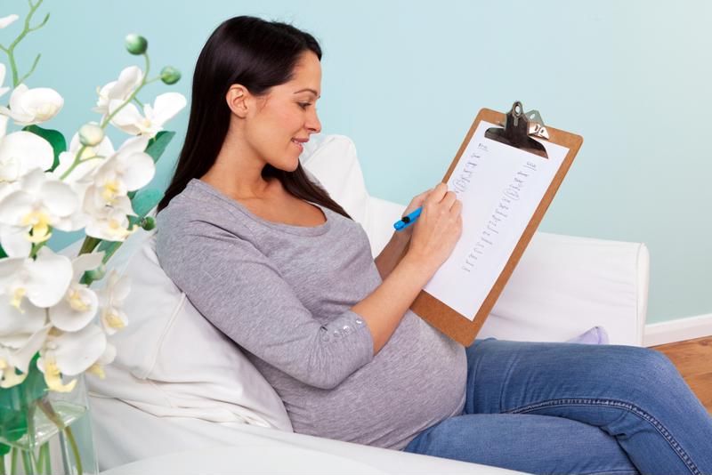 A pregnant woman taking notes on a clipboard.