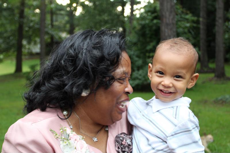 A grandmother holds her grandson, both smiling.