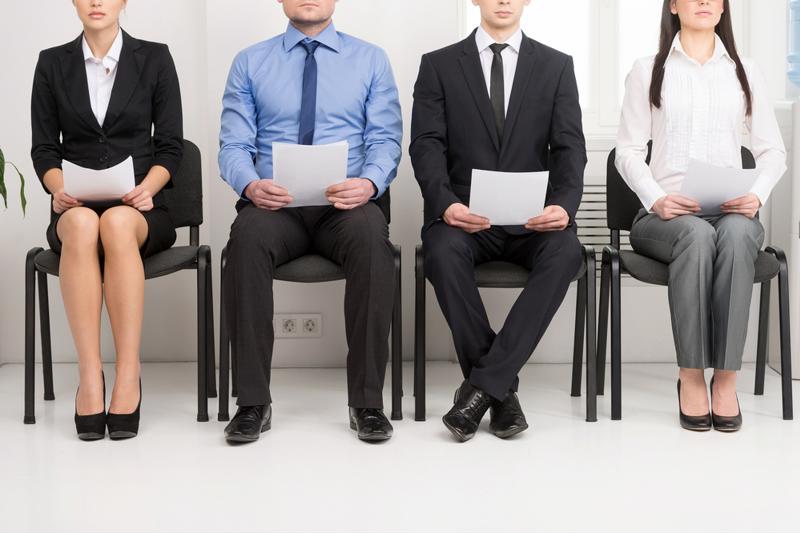 Four business people sit and await interviews with their resumes in hand