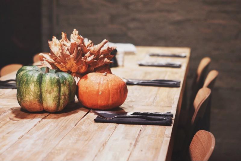 A table set with forks and knives. An arrangement of pumpkins and autumn leaves acts as a centerpiece.