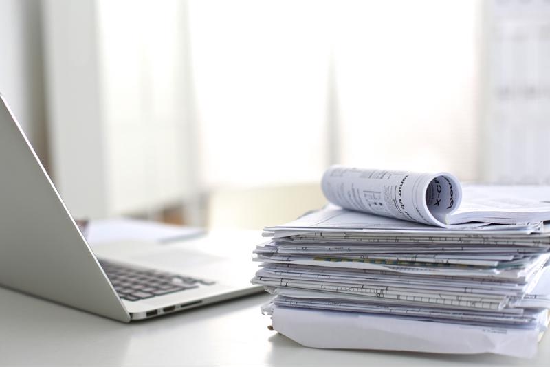 Image of a desk with tax documents, a calculator, and a laptop. The documents include a tax return form, receipts, and a pen.