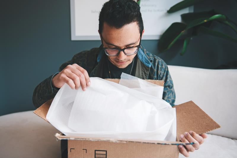 Man opening cardboard box with tissue paper inside. 
