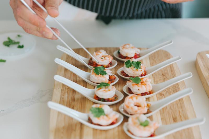 A group of shrimp plated carefully in flat-bottomed soup spoons.