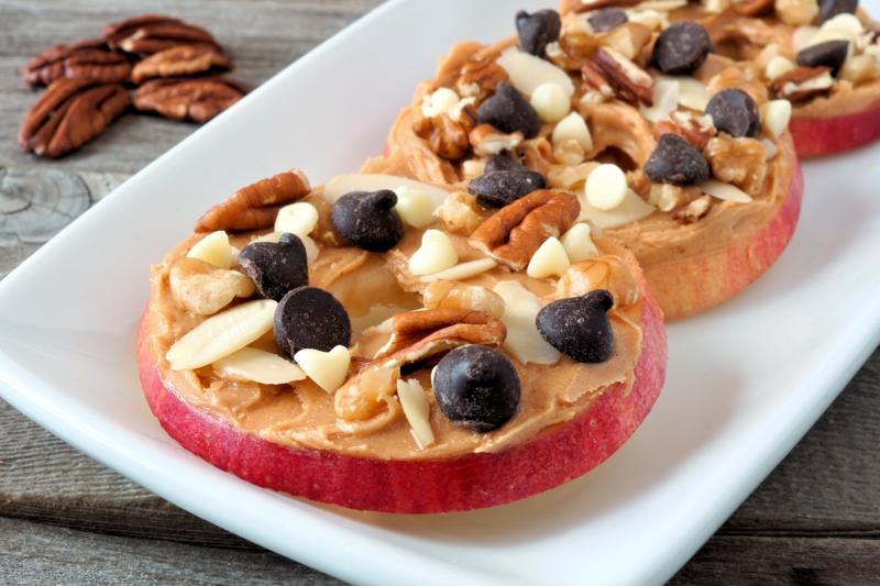 An appetizer of apple slices, peanut butter, nuts and chocolate chips on a long plate.
