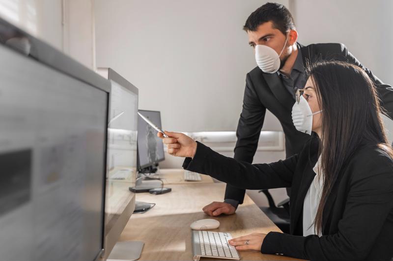 Two office workers wearing face masks to minimize risk of COVID-19 transmission.
