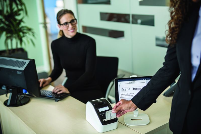 An administration worker using a visitor management system by printing a label for a guest.