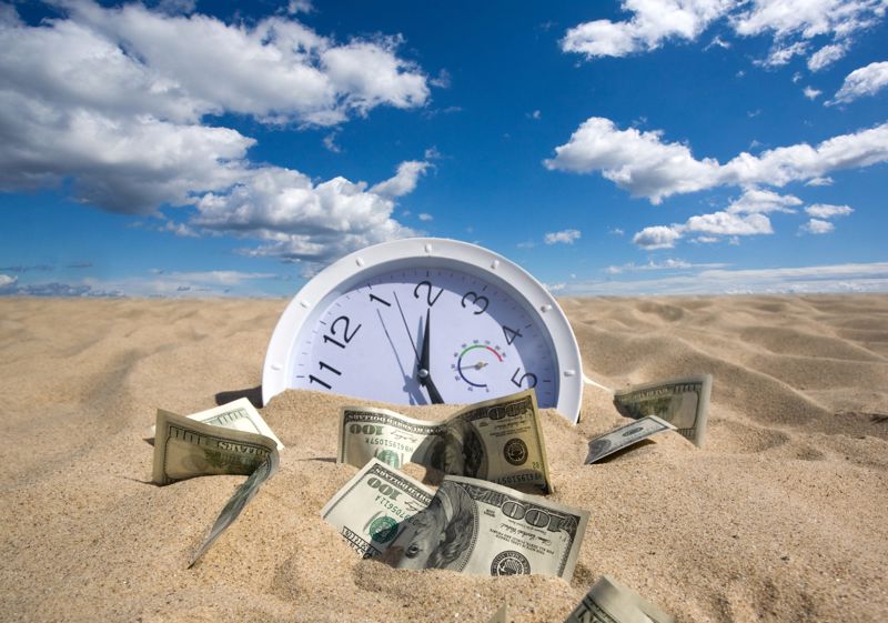 White clock in sand surrounded by paper money.