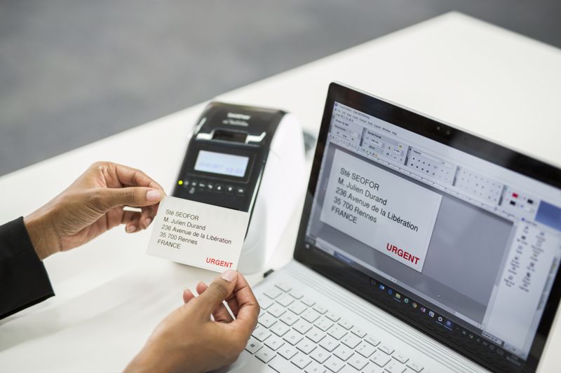 A Brother QL label printer next to a laptop printing off labels.