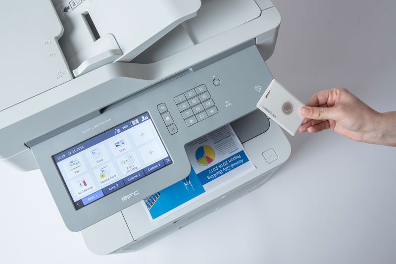 A hand holding a keycard over a multi-function printer