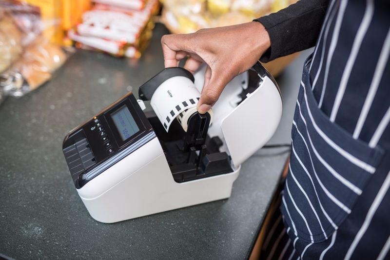 A Brother label printer with its tape roll being replaced by a worker in a bakery