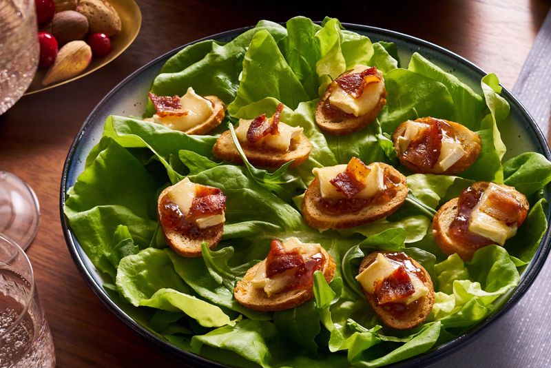 Bacon fig jam crostinis sit on a bead of lettuce on a plate