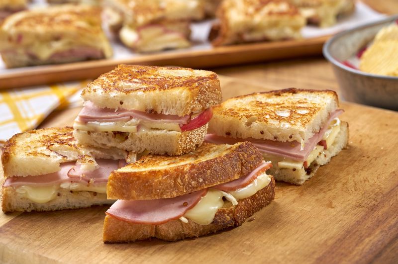 Stacks of ham and brie grilled cheeses sit on a table