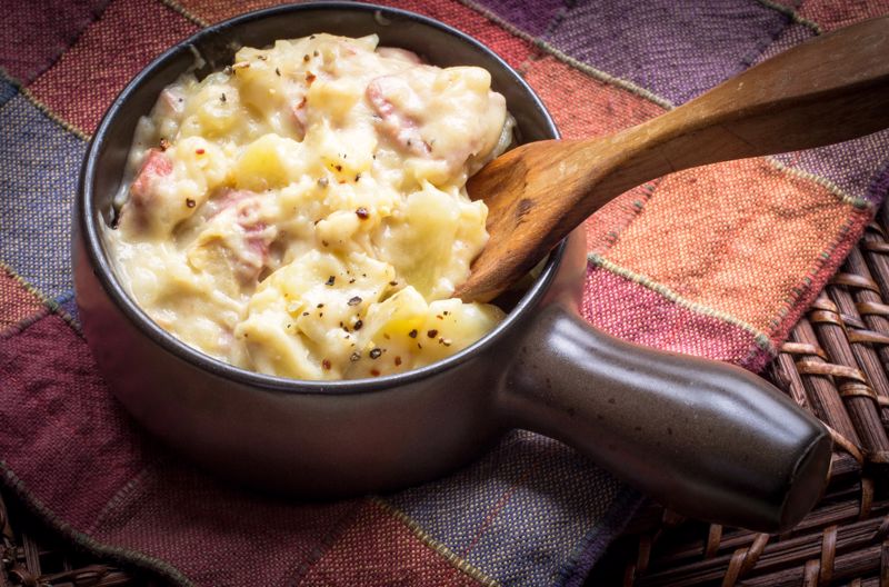 Someone mixes scalloped potatoes in a pot with a spoon 