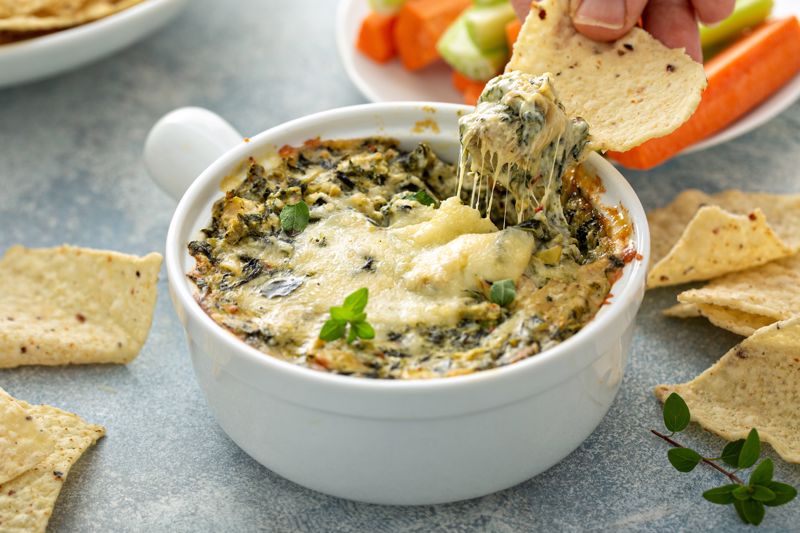 Someone dips a chip into spinach artichoke dip