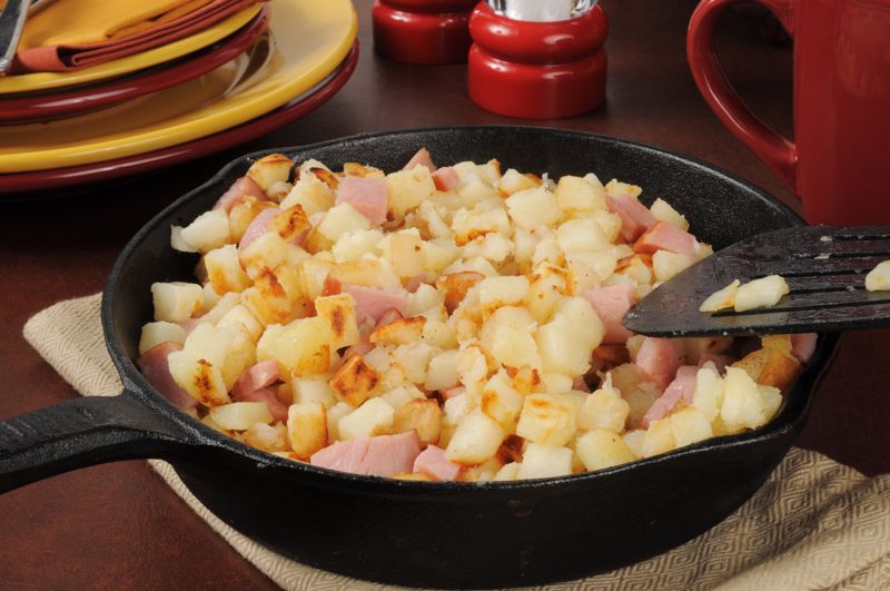 Someone mixes potatoes and other ingredients in a skillet