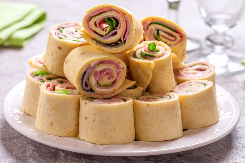 Ham and cheese roll-up starters sit stacked on a plate