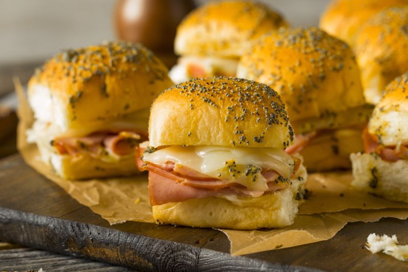 Ham and cheese sliders on Hawaiian rolls sit on a wooden board
