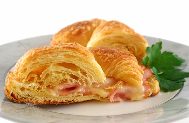 A flaky crescent is partially open revealing ham and cheese on the inside