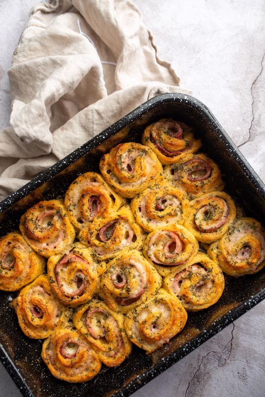 A tray full of baked ham and cheese pinwheels sits on a table