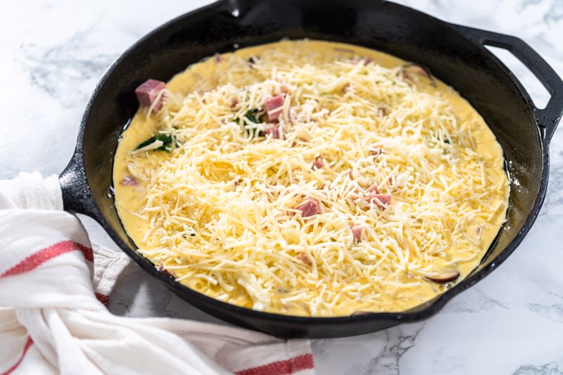 The ingredients for a ham and cheese egg frittata are gathered in an iron skillet