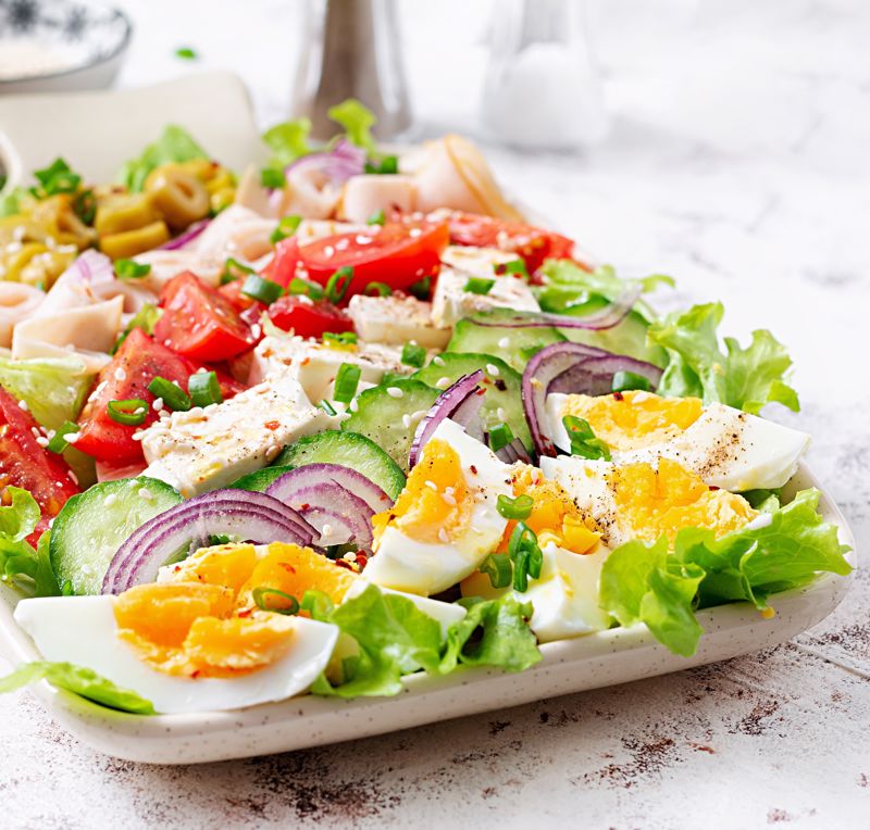 The ingredients of cobb salad with ham are neatly laid out on a plate