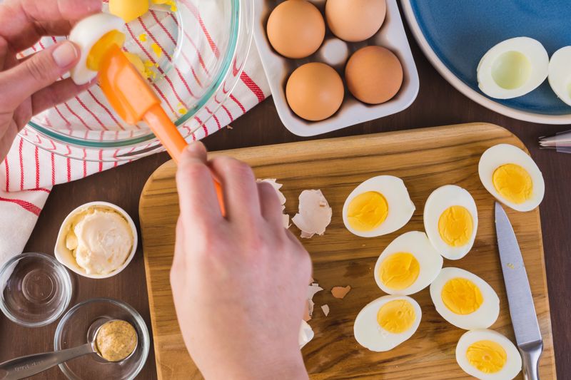 Someone scoops out the yolk of a hard-boiled egg for deviled eggs