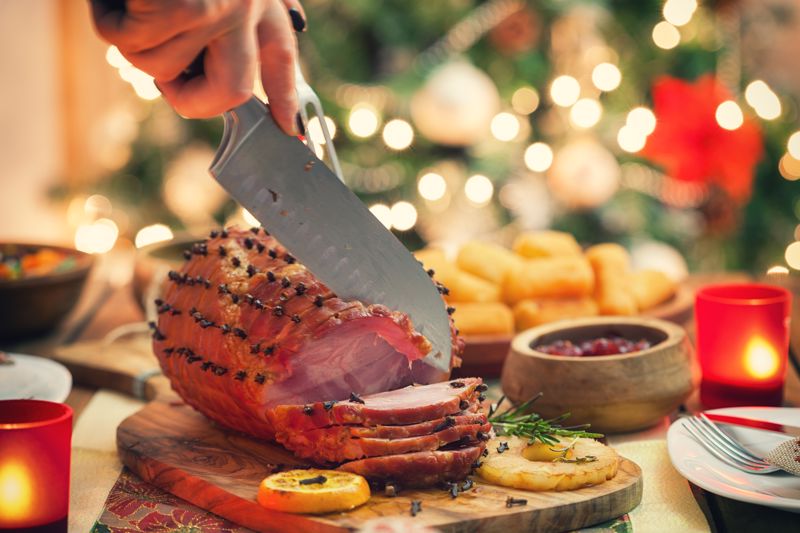 Someone carves a holiday ham on a wooden cutting board