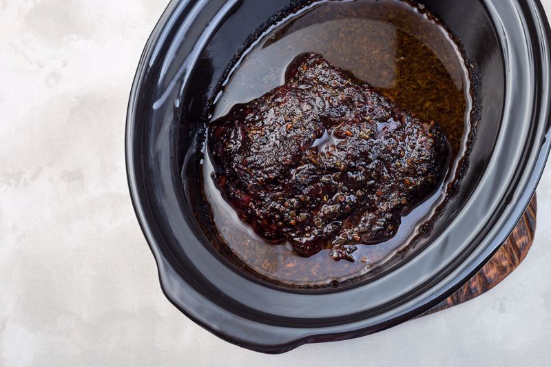 A cut of pork sits in a marinade in a slow cooker