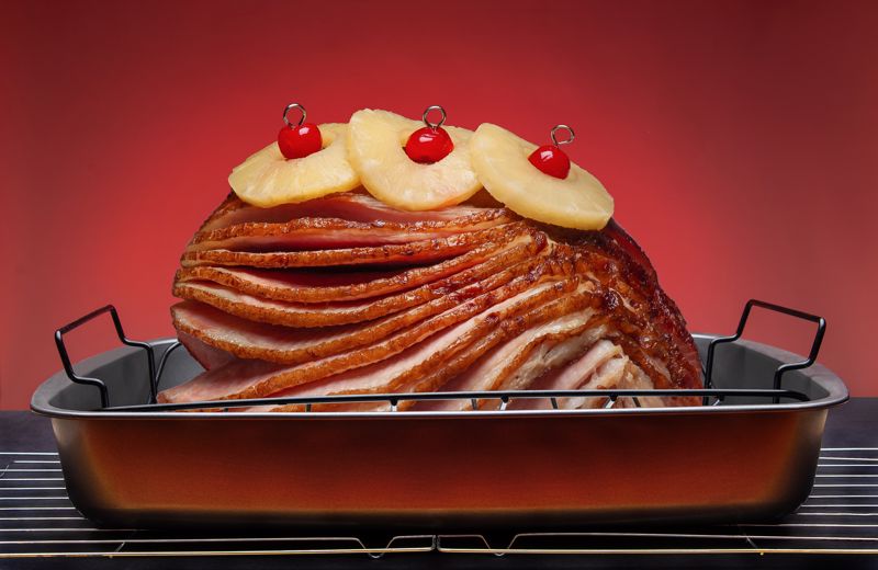 A sliced ham topped with pineapples and cherries sits in a pan