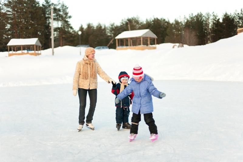A mother ice skating with her two young kids. 